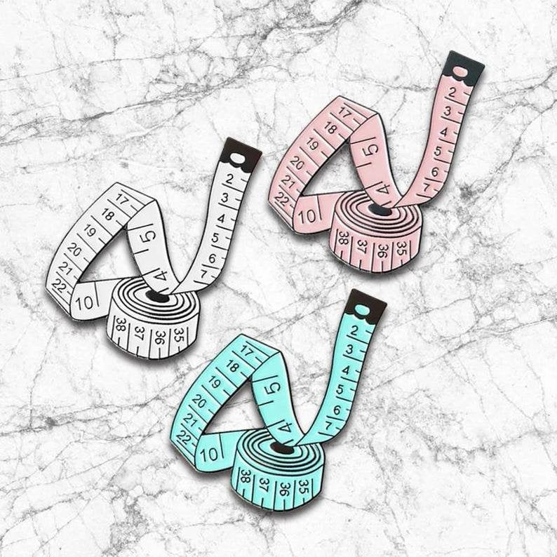 Enameled sewing tape pin in white, blue, and pink color options, perfect gift for sewing lovers and crafters