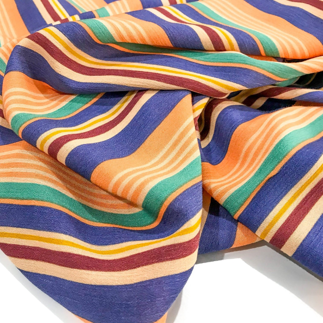 Rayon Crepe Cabana Stripe fabric in peach, periwinkle, and mint colors with flowing drape