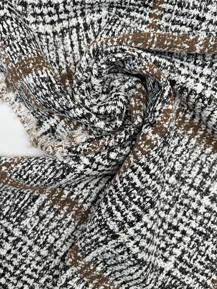 Close-up of Italian tweed fabric in wool and cotton blend, featuring white, black, and brown tones, ideal for coats, suits, and structured skirts.