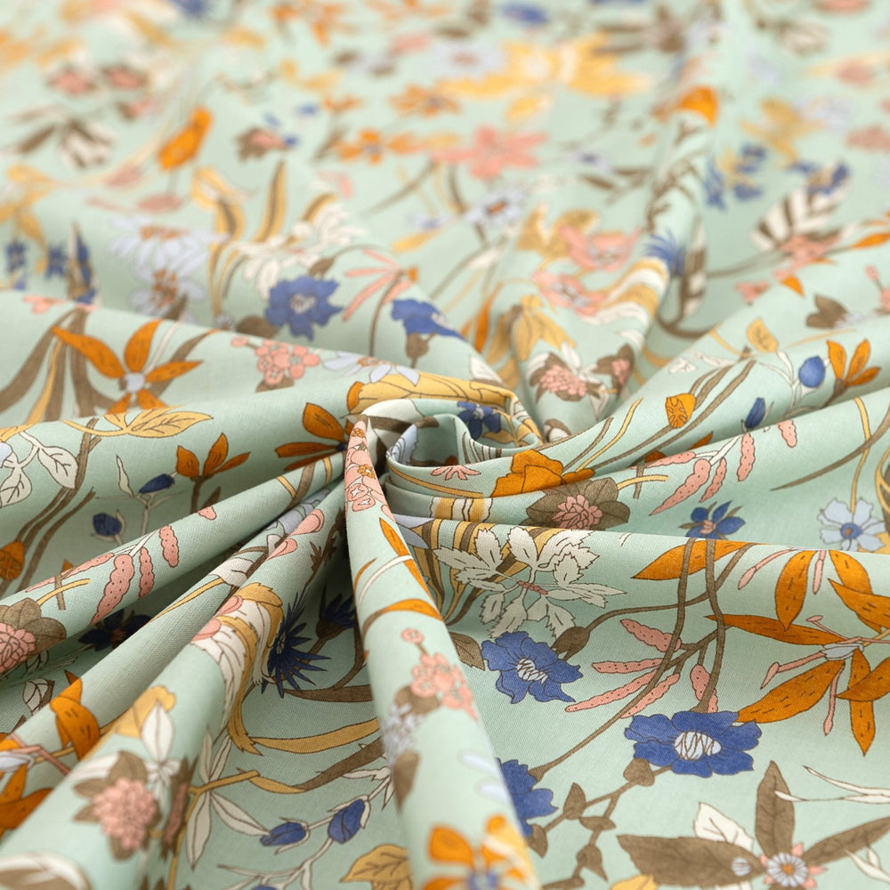 Rolls of floral fabric with orange, blue, and brown flowers on a light green background.