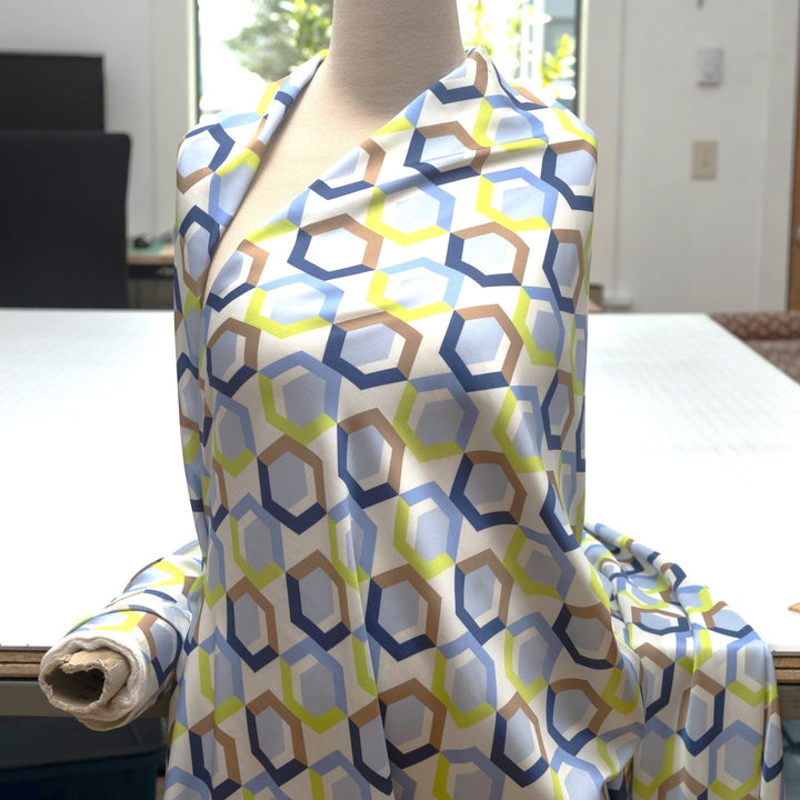 Viscose Sateen Prism Play fabric with geometric shapes in white, blue, and green, luxurious smooth drape and subtle sheen