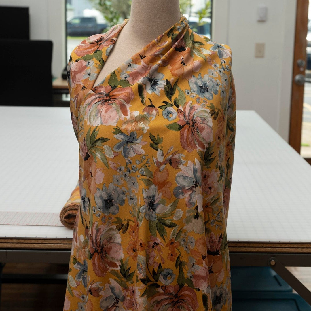 Rayon Poplin Golden Sunset Bloom fabric with marigold base, pumpkin, blue, and olive floral accents – 100% rayon sewing material