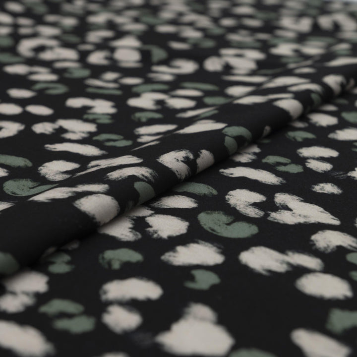 Rayon Challis fabric in black with scattered olive dots, perfect for sewing blouses, dresses, and skirts.