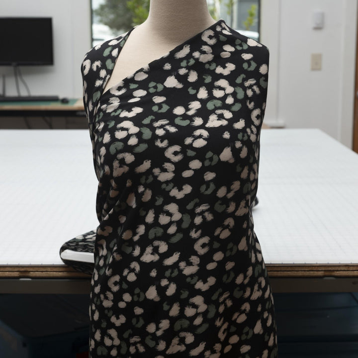 Rayon Challis fabric in black with scattered olive dots, perfect for sewing blouses, dresses, and skirts.