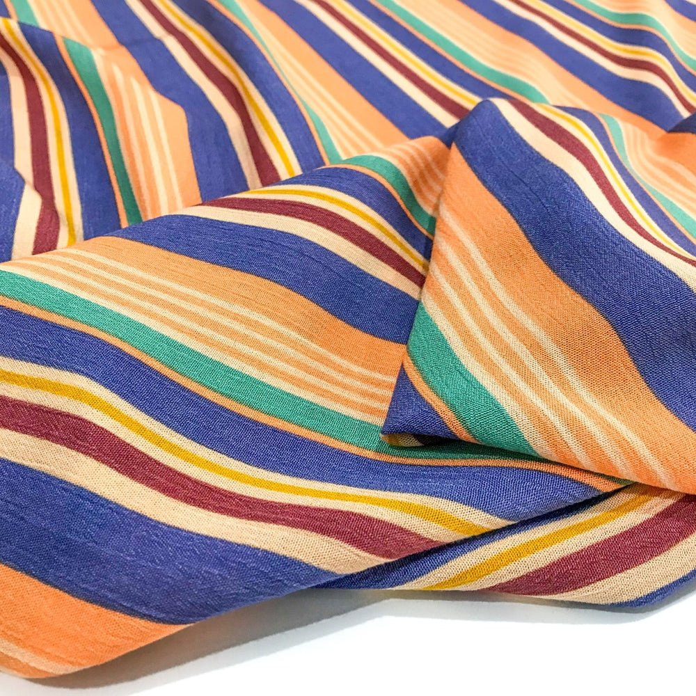 Rayon Crepe Cabana Stripe fabric in peach, periwinkle, and mint colors with flowing drape