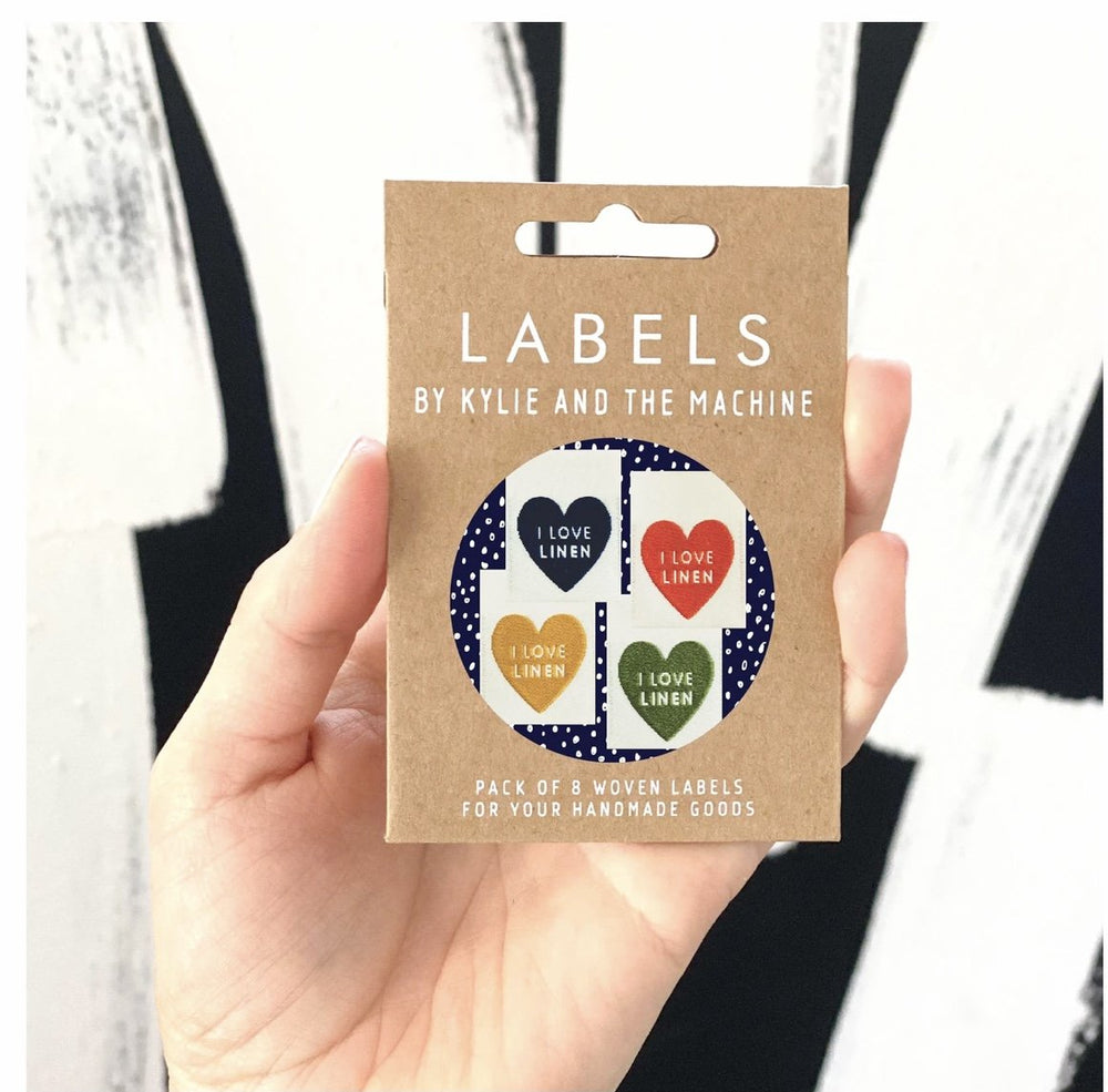 "Kylie and the Machine I Love Linen woven label – off-white background with hearts in mustard yellow, burnt orange, navy, and deep green"

