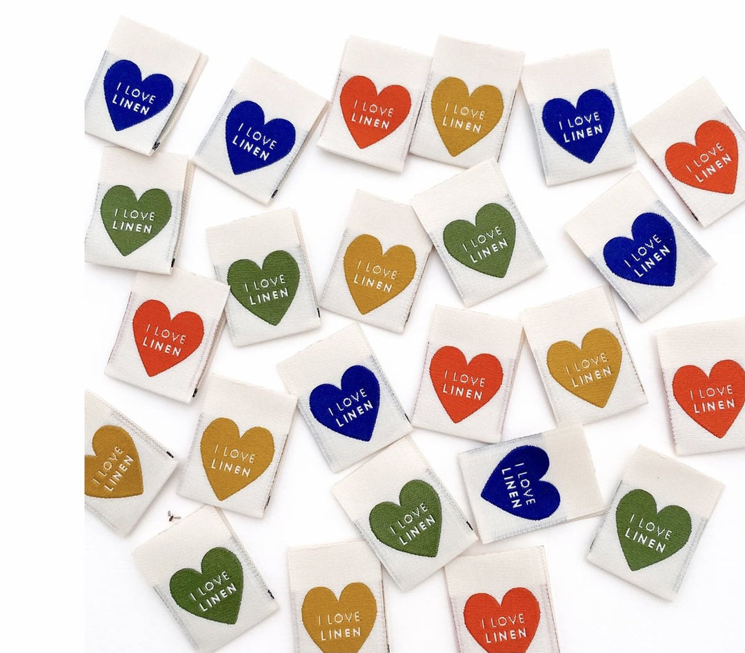 "Kylie and the Machine I Love Linen woven label – off-white background with hearts in mustard yellow, burnt orange, navy, and deep green"

