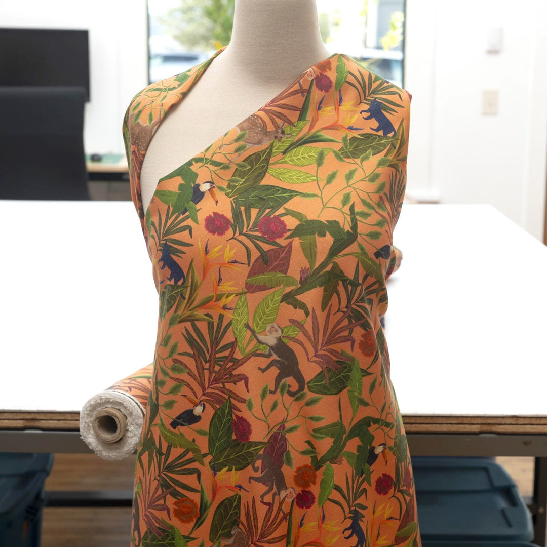 "Italian linen fabric in vibrant orange with jungle print – features monkeys, birds, and deer on lightweight linen, perfect for shirts, dresses, and skirts"

