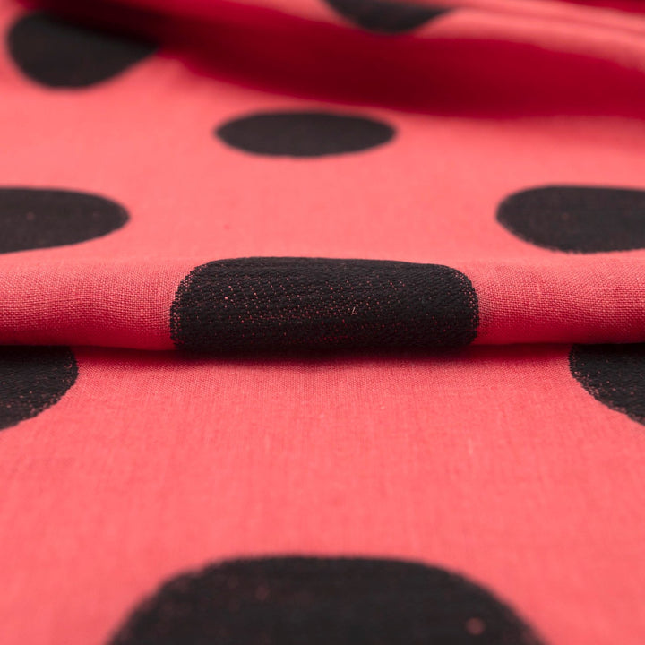 Sunset red-orange linen fabric with large 3-inch black embroidered polka dots, soft drape, and breathable medium-weight texture for stylish garments.

