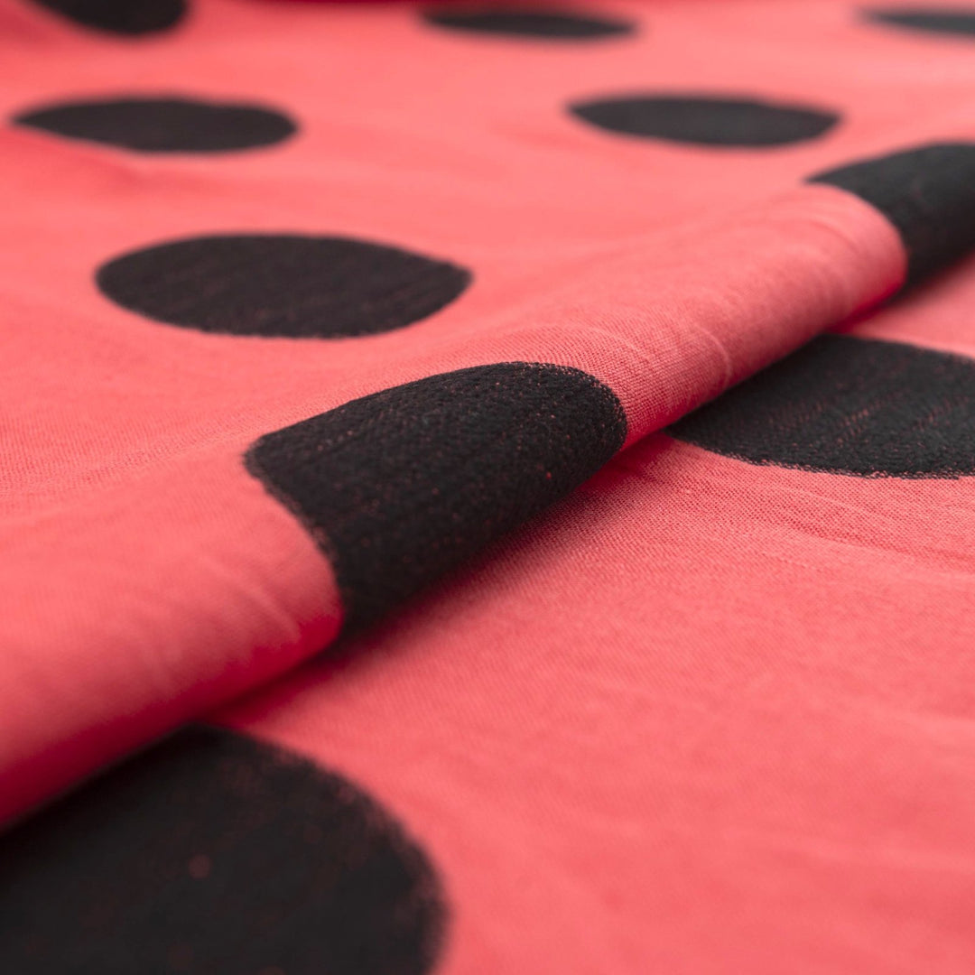 Sunset red-orange linen fabric with large 3-inch black embroidered polka dots, soft drape, and breathable medium-weight texture for stylish garments.

