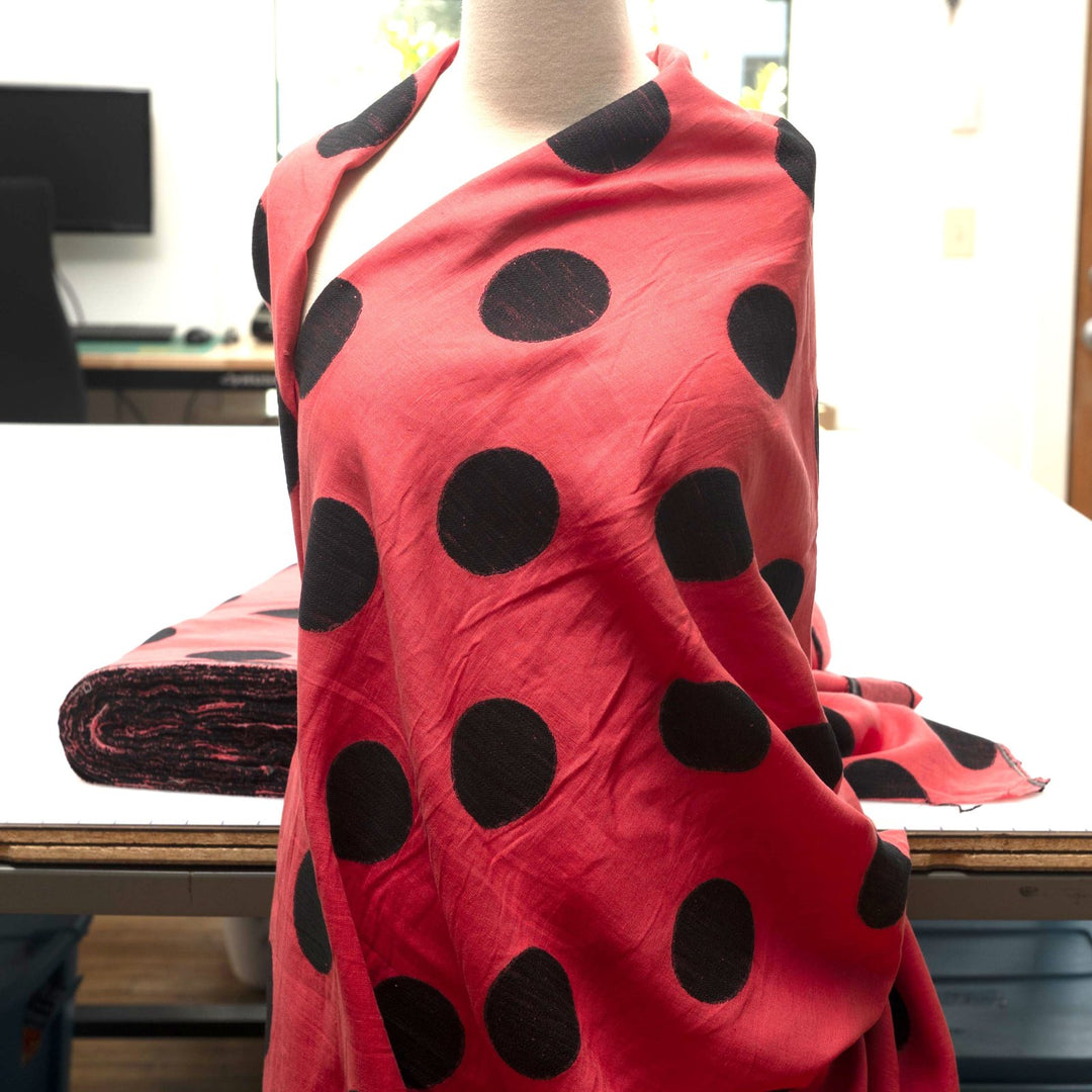 Sunset red-orange linen fabric with large 3-inch black embroidered polka dots, soft drape, and breathable medium-weight texture for stylish garments.

