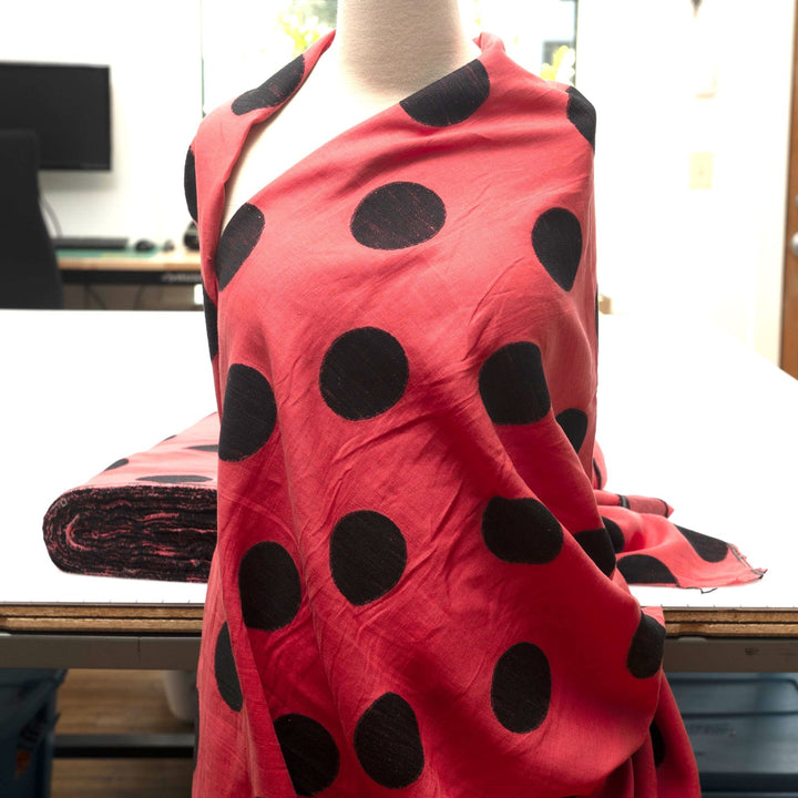 Sunset red-orange linen fabric with large 3-inch black embroidered polka dots, soft drape, and breathable medium-weight texture for stylish garments.

