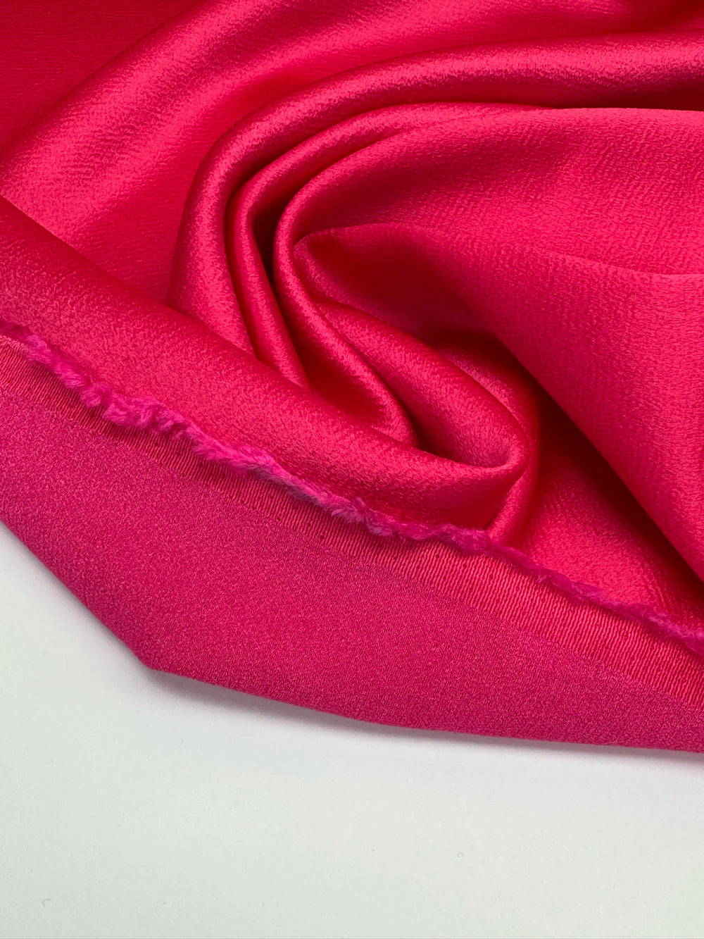 Luxurious Rayon Satin fabric in bright pink with a textured finish. Made from 65% Acetate and 35% Rayon/Viscose. Ideal for dresses, skirts, and blouses.