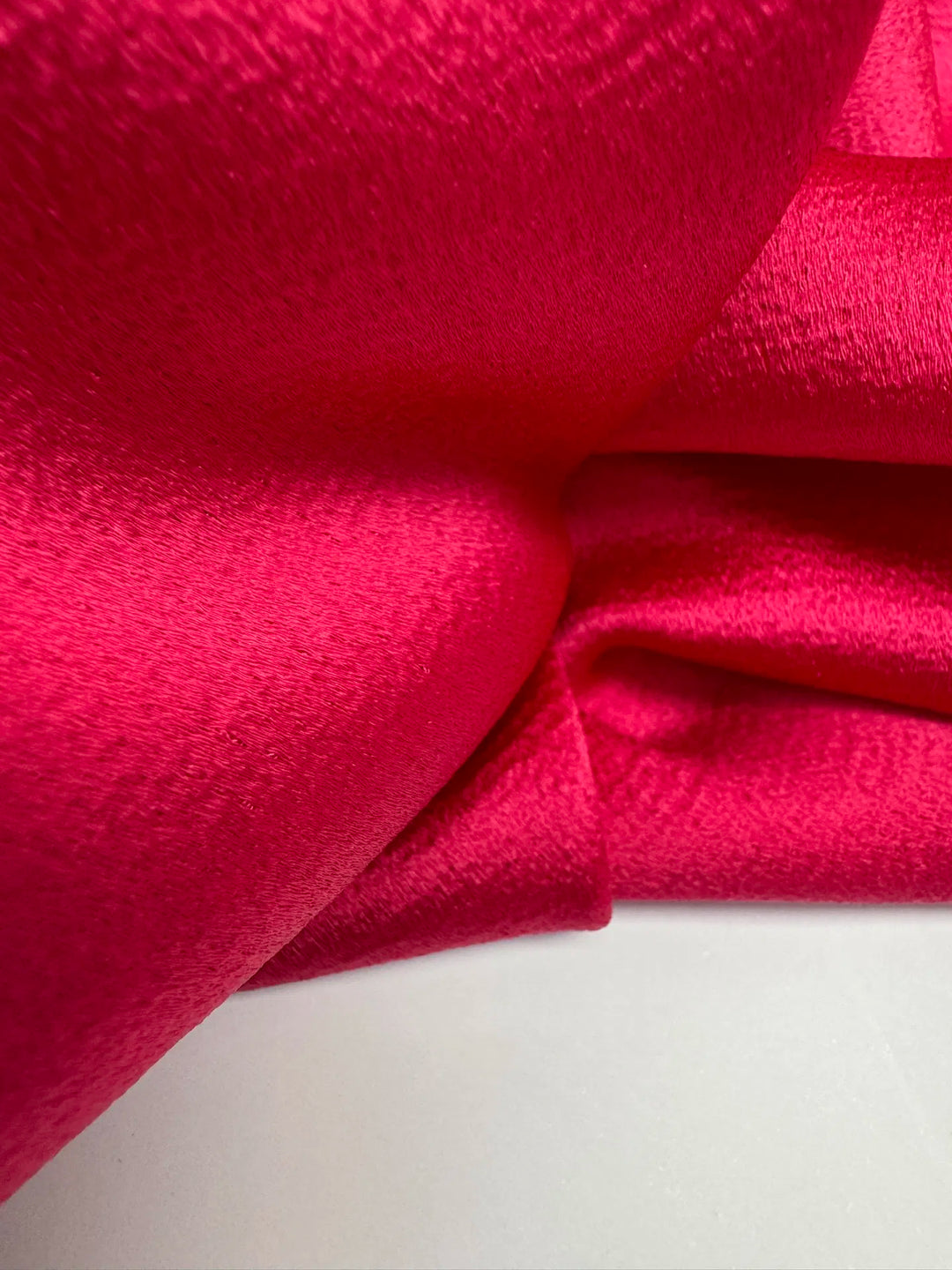 Luxurious Rayon Satin fabric in bright pink with a textured finish. Made from 65% Acetate and 35% Rayon/Viscose. Ideal for dresses, skirts, and blouses.