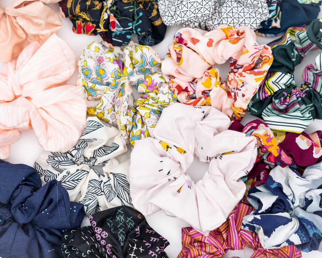 A collection of colorful, soft fabric scrunchies in various patterns and designs, perfect for matching with accessories like robes and makeup bags.