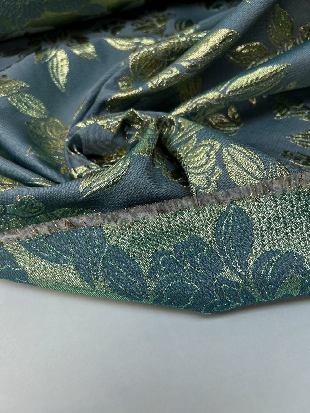 French jacquard fabric with metallic leaf pattern in teal and gold, polyester lurex acrylic blend, ideal for bridal gowns, evening dresses, and formalwear.