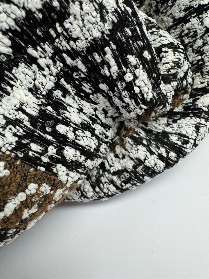 Close-up of Italian tweed fabric in wool and cotton blend, featuring white, black, and brown tones, ideal for coats, suits, and structured skirts.