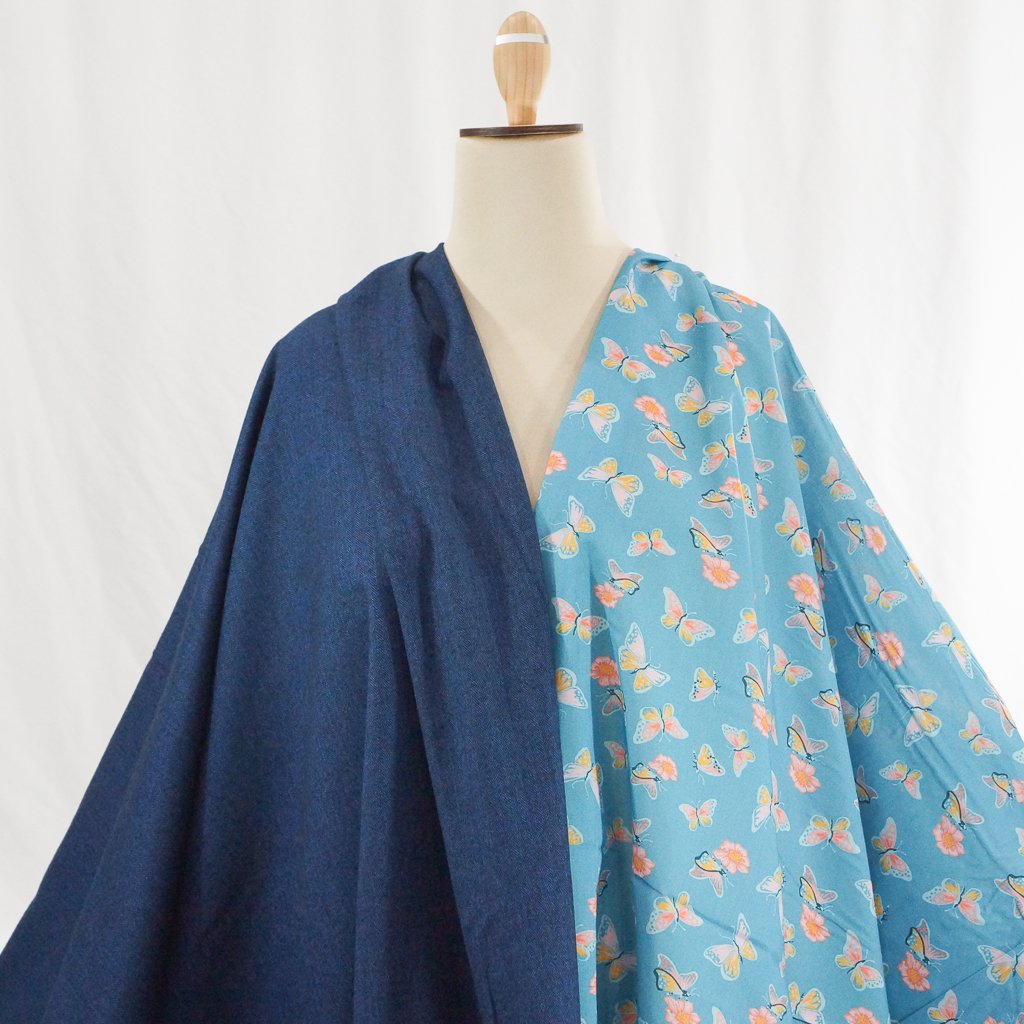 Close-up of Organic Cotton Lawn – Butterflies on Blue fabric featuring whimsical butterfly print on a soft sky-blue background.
