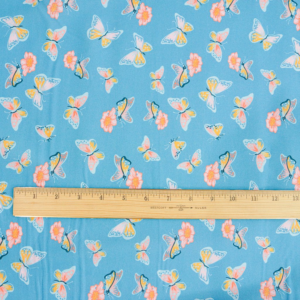 Close-up of Organic Cotton Lawn – Butterflies on Blue fabric featuring whimsical butterfly print on a soft sky-blue background.