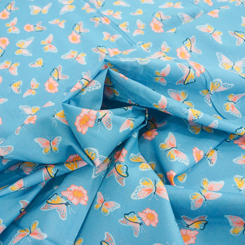 Close-up of Organic Cotton Lawn – Butterflies on Blue fabric featuring whimsical butterfly print on a soft sky-blue background.