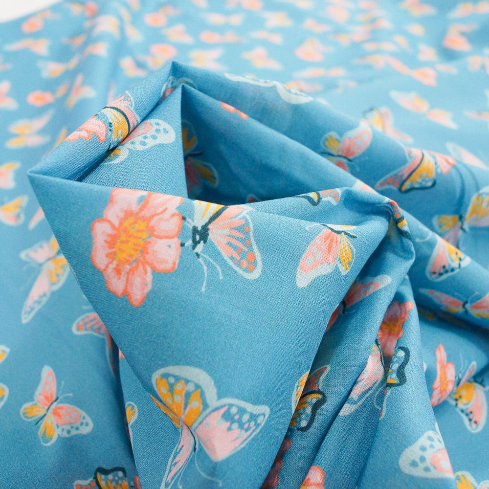 Close-up of Organic Cotton Lawn – Butterflies on Blue fabric featuring whimsical butterfly print on a soft sky-blue background.