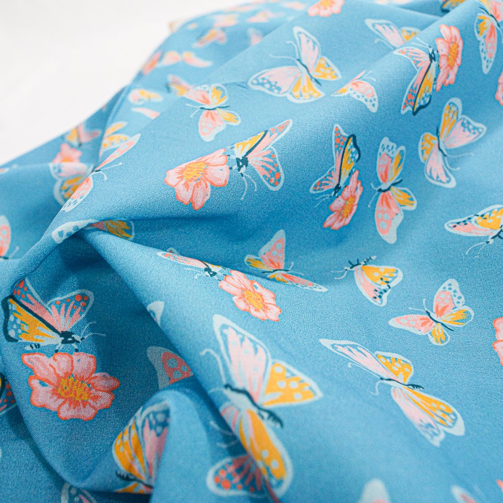 Close-up of Organic Cotton Lawn – Butterflies on Blue fabric featuring whimsical butterfly print on a soft sky-blue background.