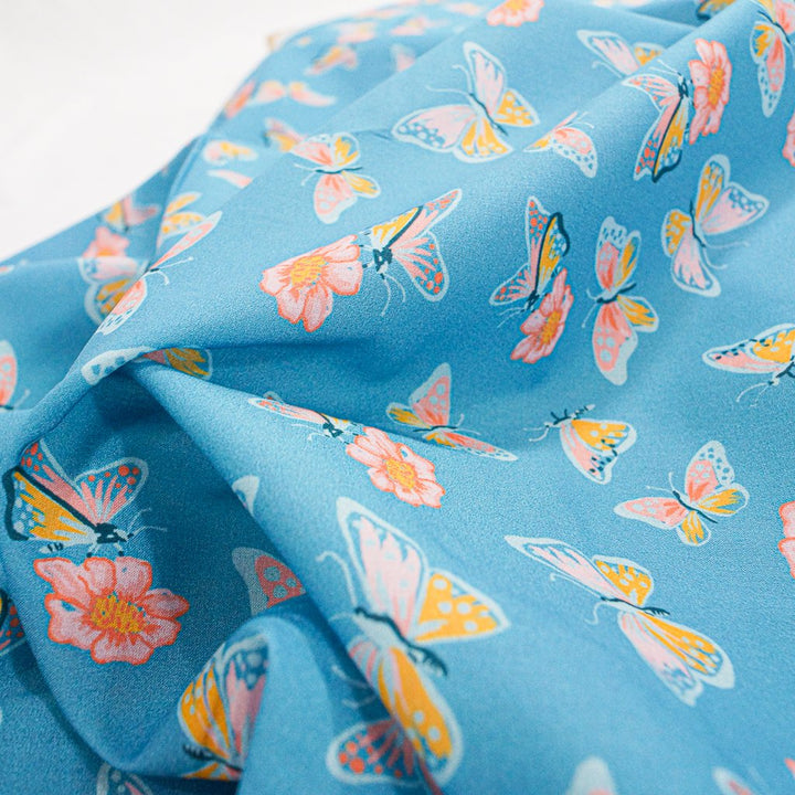 Close-up of Organic Cotton Lawn – Butterflies on Blue fabric featuring whimsical butterfly print on a soft sky-blue background.