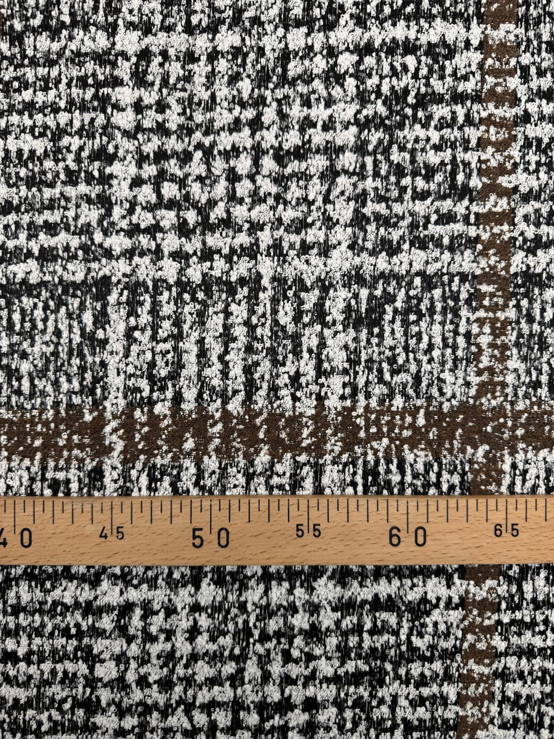 Close-up of Italian tweed fabric in wool and cotton blend, featuring white, black, and brown tones, ideal for coats, suits, and structured skirts.