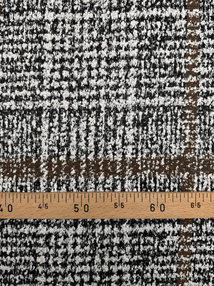 Close-up of Italian tweed fabric in wool and cotton blend, featuring white, black, and brown tones, ideal for coats, suits, and structured skirts.