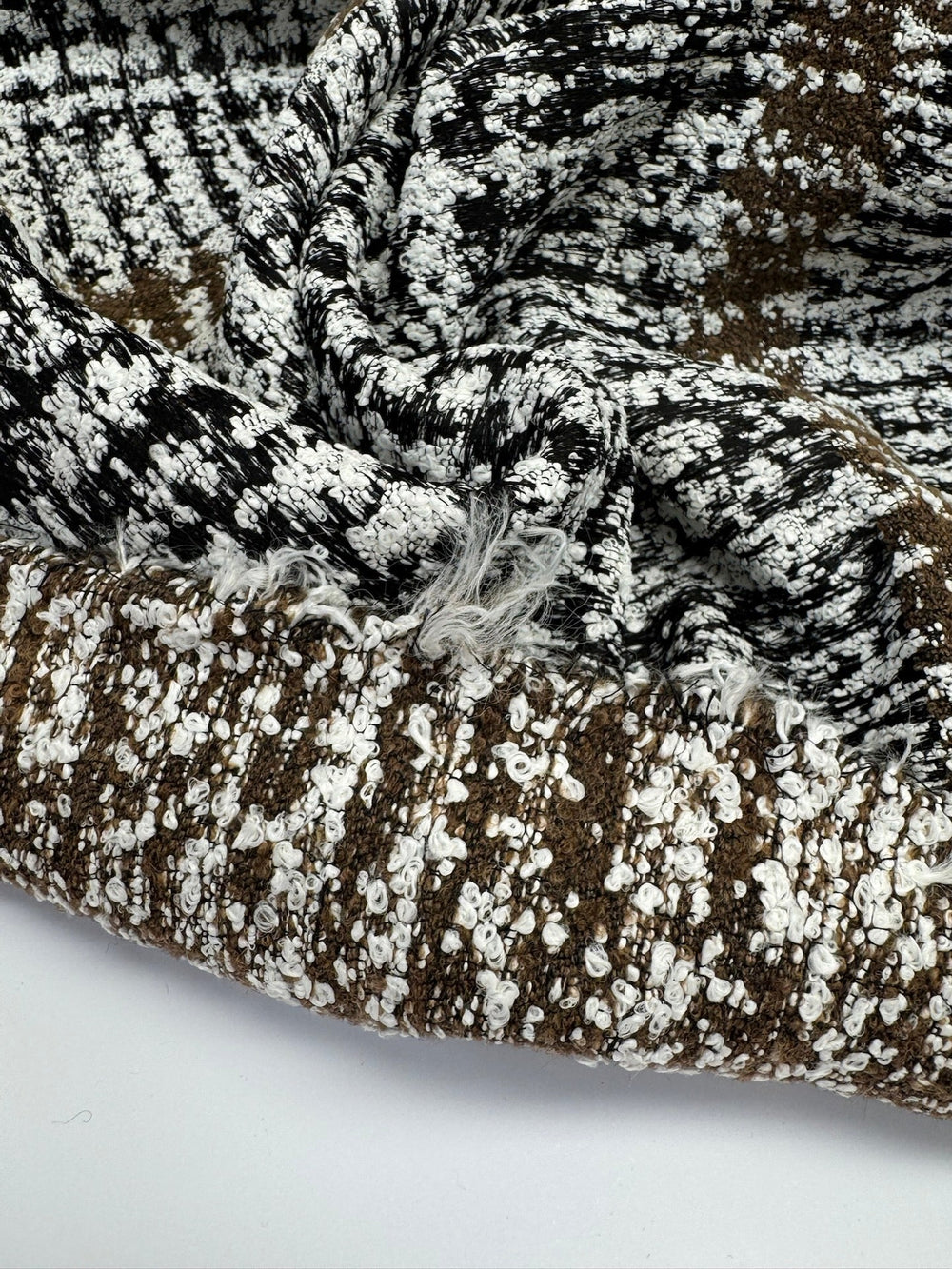 Close-up of Italian tweed fabric in wool and cotton blend, featuring white, black, and brown tones, ideal for coats, suits, and structured skirts.