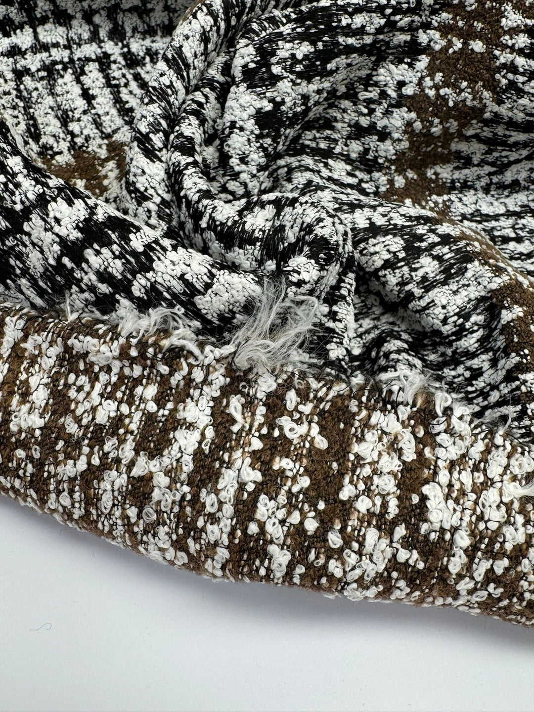Close-up of Italian tweed fabric in wool and cotton blend, featuring white, black, and brown tones, ideal for coats, suits, and structured skirts.