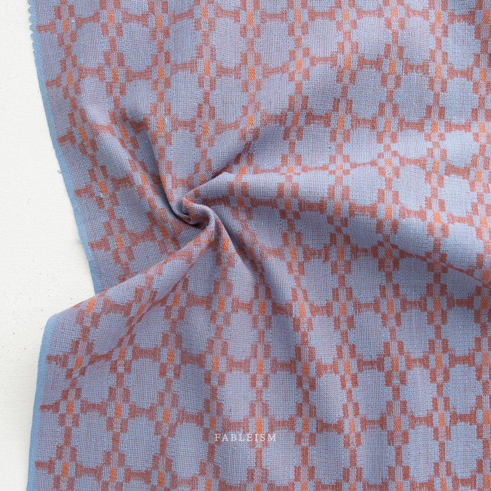 Cotton woven fabric in monarch grove design with blue and rust tones – 100% cotton material for shirts, blouses, dresses, and skirts.
