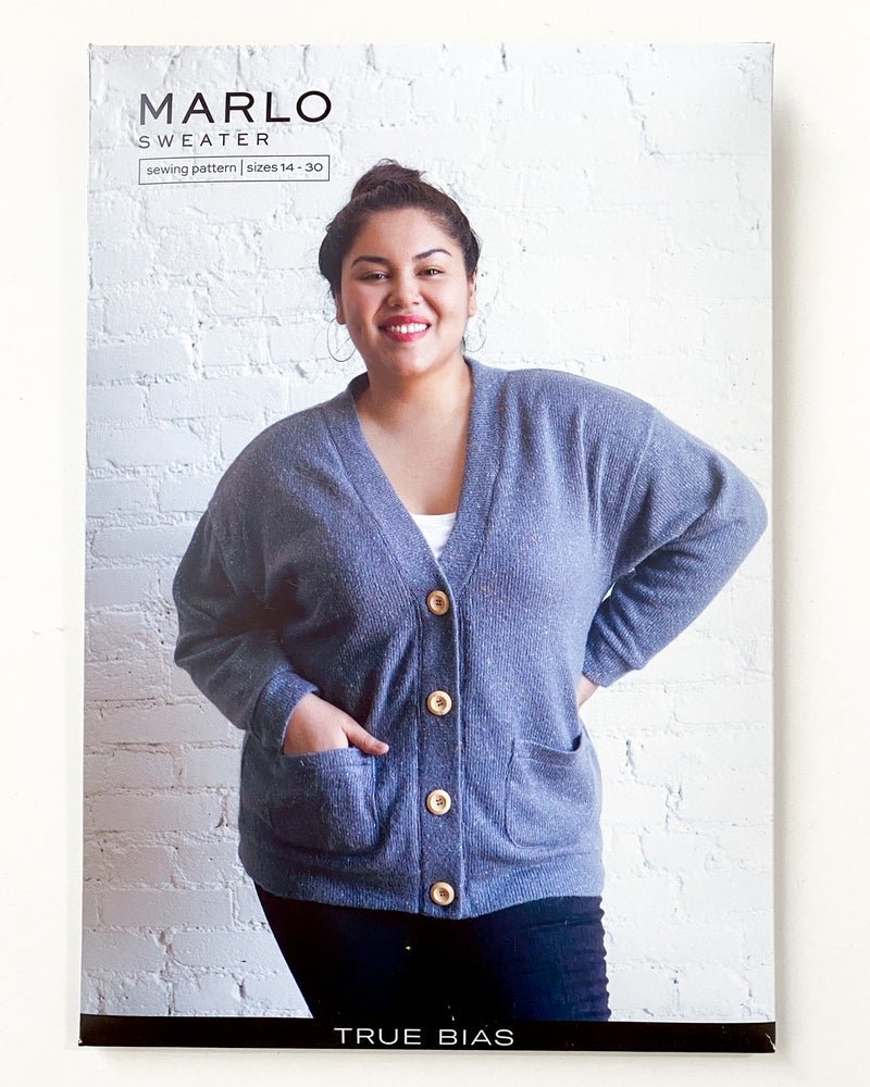 True Bias Marlo Sweater in cozy medium-weight knit with deep V-neck and large buttons, shown in mid-thigh length with patch pockets.