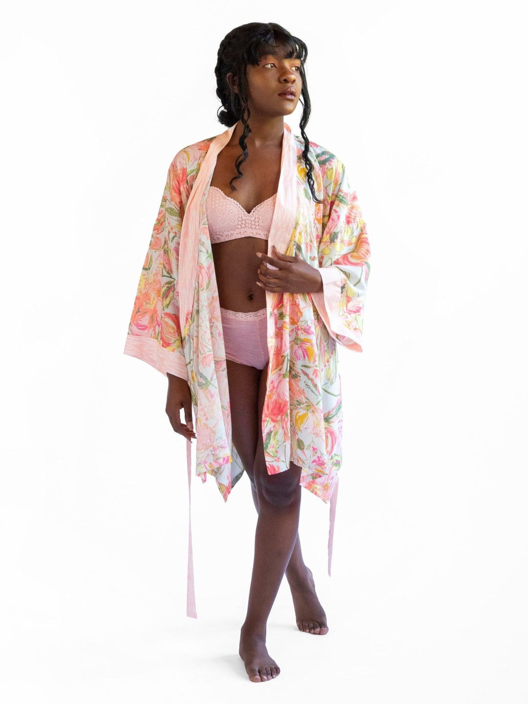 A woman wearing a watercolor floral printed robe, standing with her back turned, showcasing the luxurious Signature Robe - Bellini.