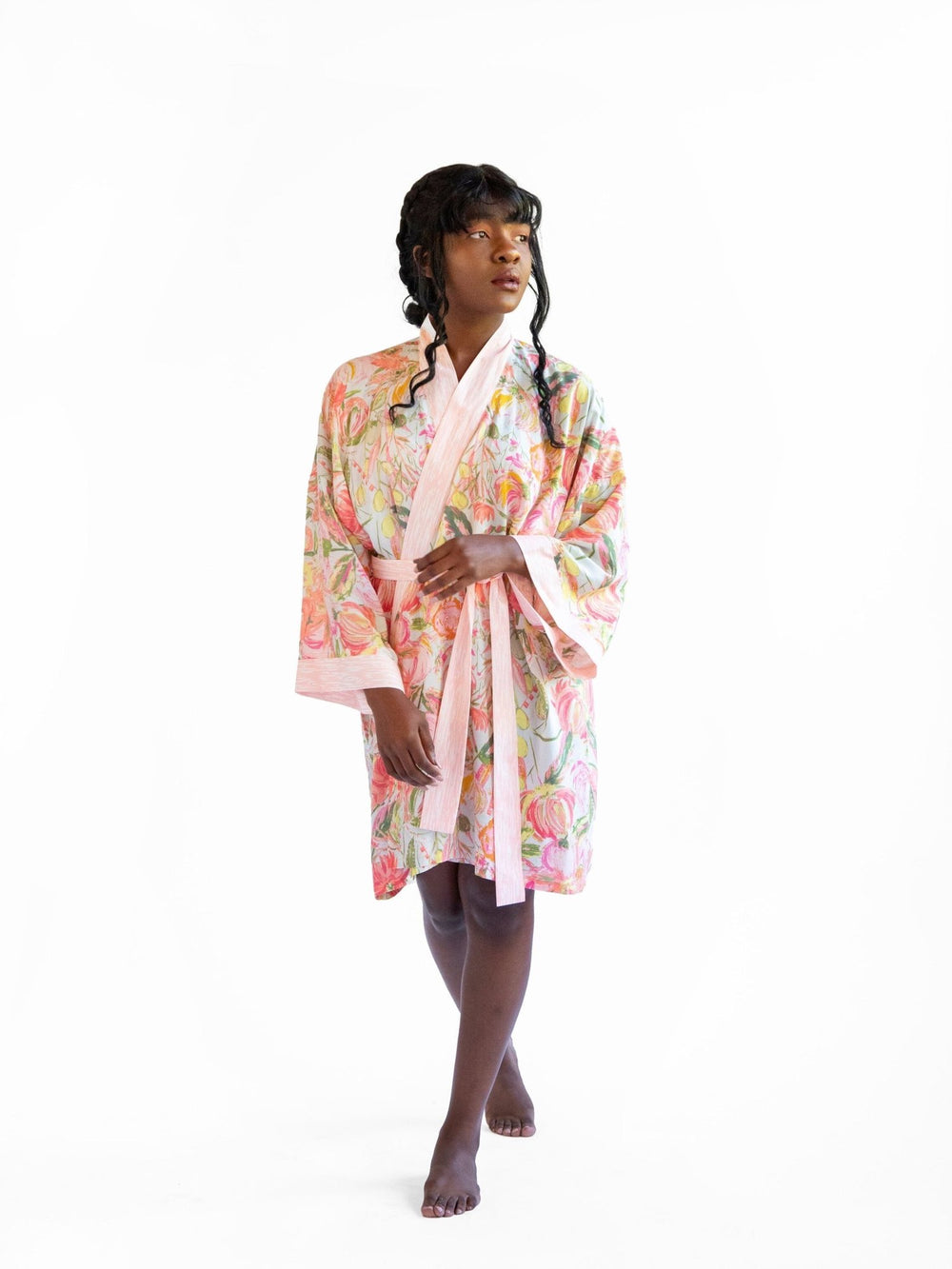 A woman wearing a watercolor floral printed robe, standing with her back turned, showcasing the luxurious Signature Robe - Bellini.