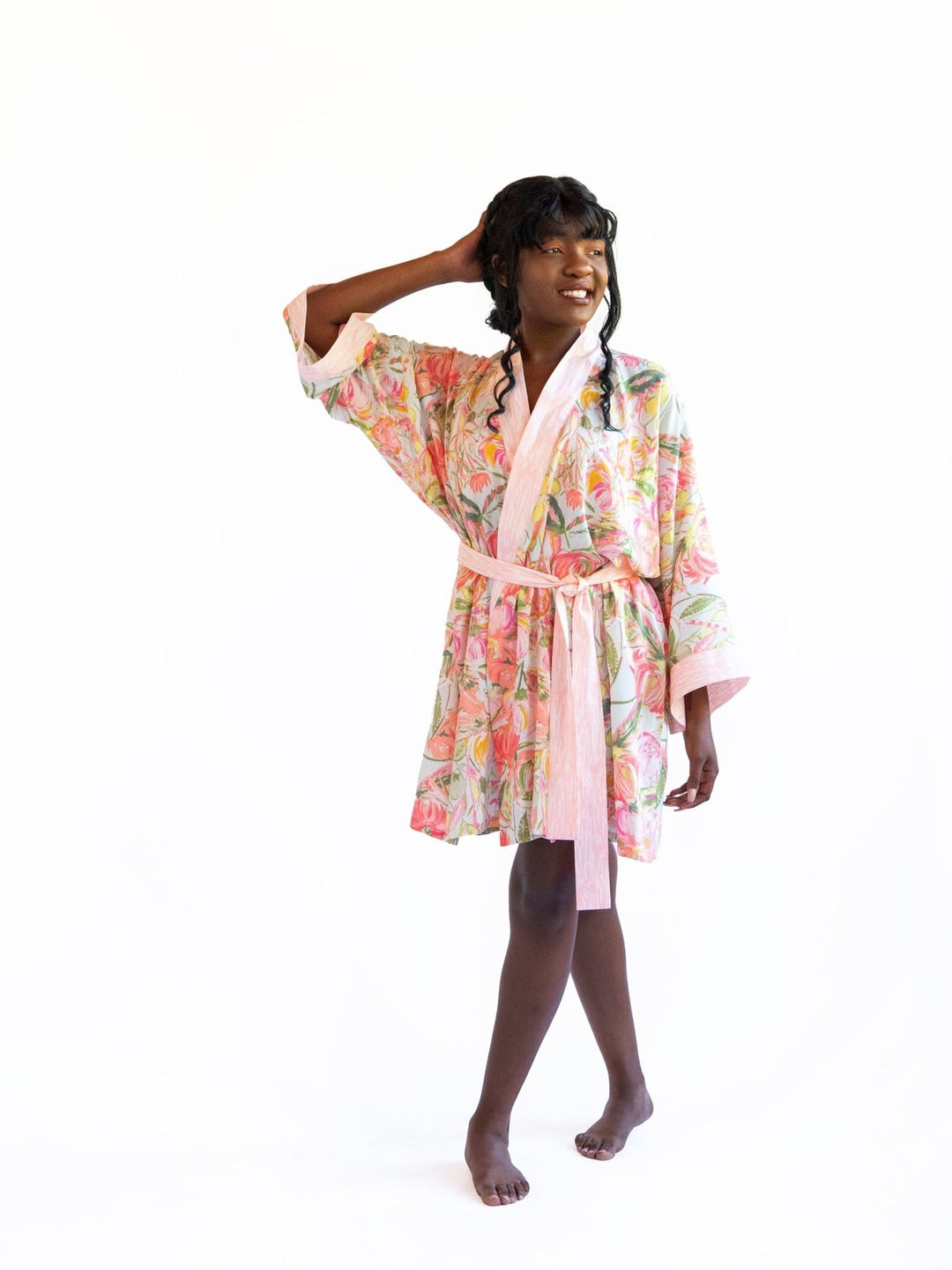 A woman wearing a watercolor floral printed robe, standing with her back turned, showcasing the luxurious Signature Robe - Bellini.